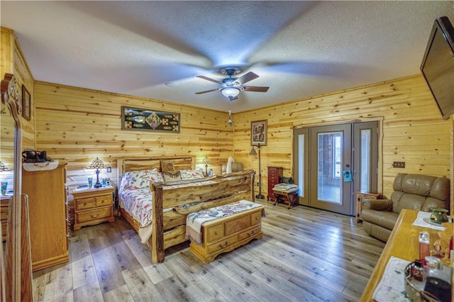 bedroom featuring ceiling fan, light wood-type flooring, a textured ceiling, and wooden walls