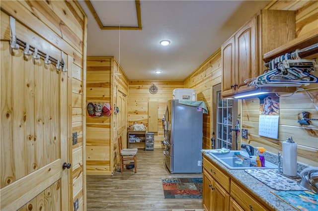 kitchen with sink, light wood-type flooring, stainless steel refrigerator, and wood walls