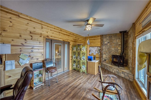 office featuring a wood stove, ceiling fan, wood-type flooring, and wood walls