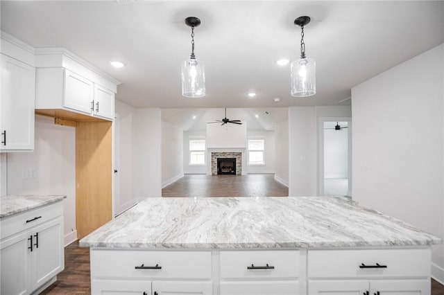 kitchen with white cabinetry, a stone fireplace, a center island, and ceiling fan