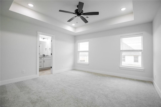 unfurnished bedroom featuring ensuite bathroom, sink, light colored carpet, ceiling fan, and a raised ceiling