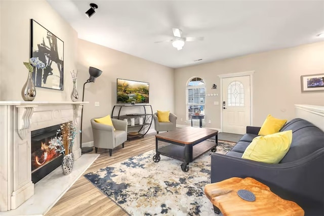 living room featuring light wood-type flooring, ceiling fan, and a premium fireplace