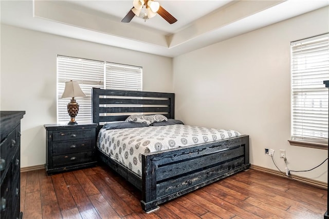 bedroom with ceiling fan, dark hardwood / wood-style floors, a tray ceiling, and multiple windows