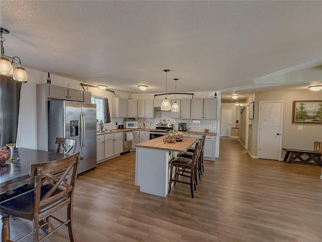 kitchen featuring appliances with stainless steel finishes, sink, a center island, butcher block countertops, and hanging light fixtures