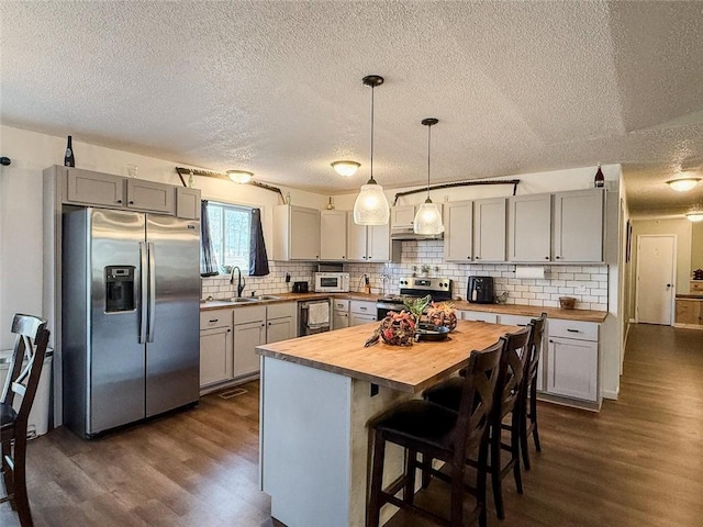 kitchen featuring wooden counters, stainless steel appliances, sink, decorative light fixtures, and a kitchen island