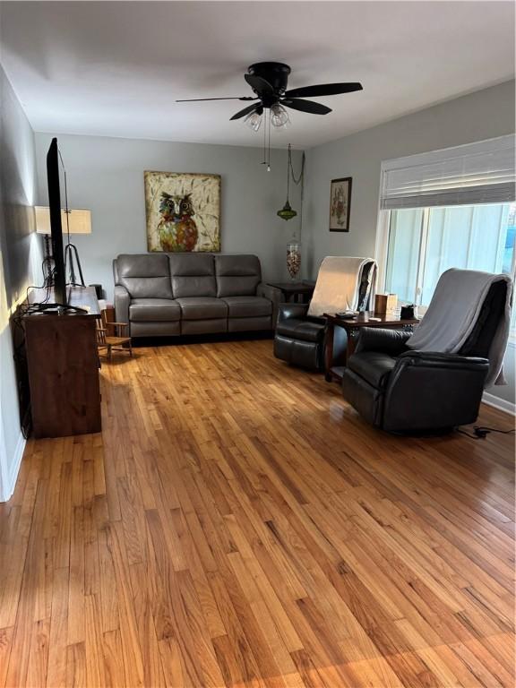 living room featuring baseboards, light wood-type flooring, and a ceiling fan