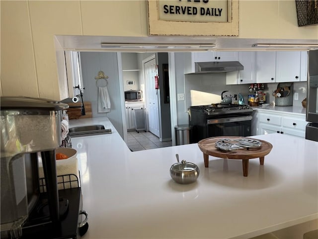 kitchen featuring tasteful backsplash, stainless steel microwave, black gas stove, under cabinet range hood, and a sink