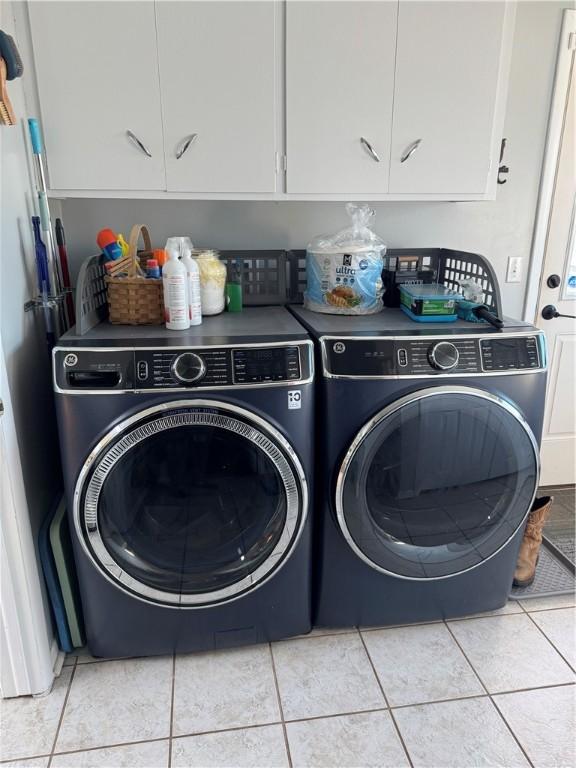 clothes washing area with light tile patterned floors, cabinet space, and washing machine and clothes dryer