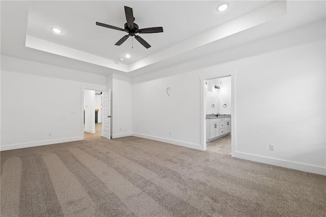 unfurnished bedroom featuring a raised ceiling, connected bathroom, ceiling fan, and light carpet