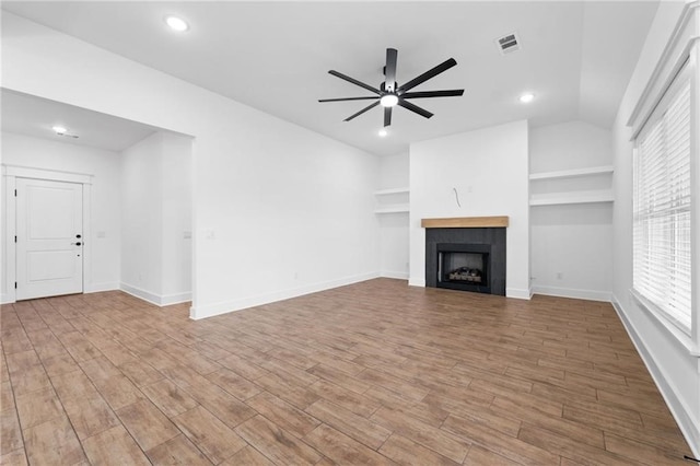 unfurnished living room featuring a tile fireplace, ceiling fan, built in features, and vaulted ceiling