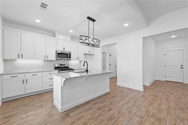 kitchen featuring a center island with sink, hanging light fixtures, sink, appliances with stainless steel finishes, and white cabinetry