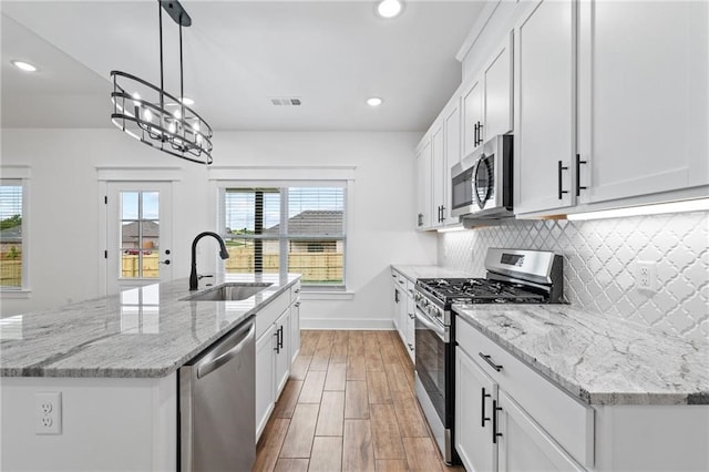 kitchen with white cabinets, a center island with sink, hanging light fixtures, sink, and appliances with stainless steel finishes