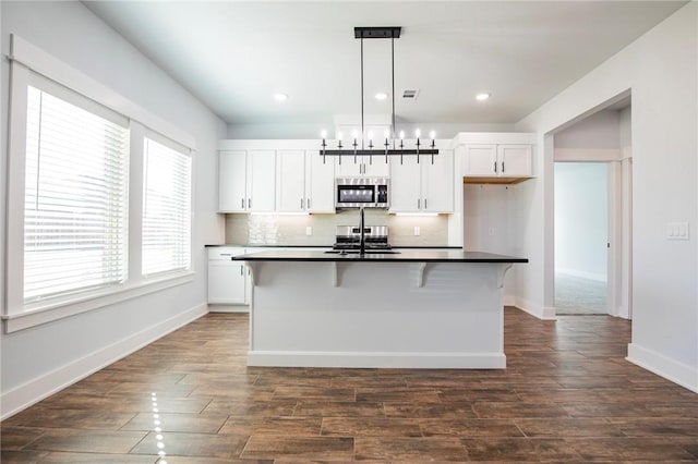 kitchen featuring white cabinetry, backsplash, range, stainless steel microwave, and dark countertops