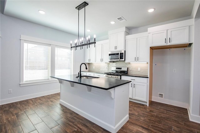 kitchen with stainless steel appliances, dark countertops, visible vents, a kitchen island with sink, and a sink