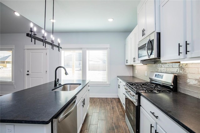 kitchen with dark countertops, a kitchen island with sink, stainless steel appliances, and a sink