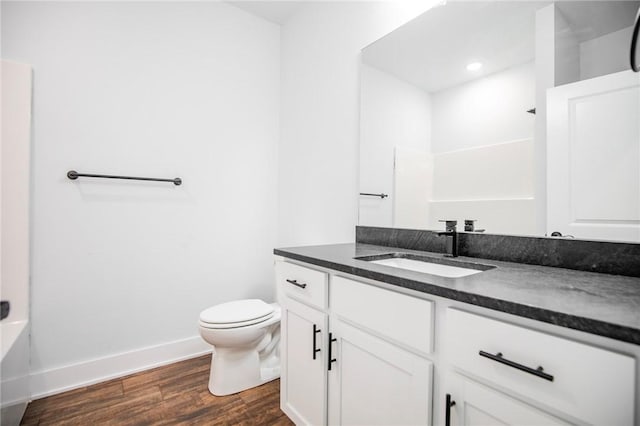 bathroom featuring baseboards, toilet, wood finished floors, vanity, and a bath