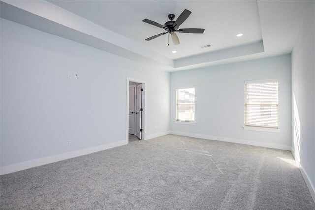 unfurnished room with light colored carpet, a raised ceiling, visible vents, and baseboards