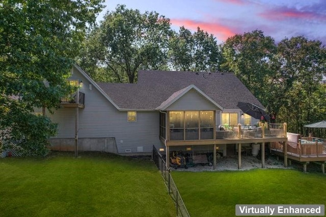 back house at dusk with a lawn, a sunroom, and a deck