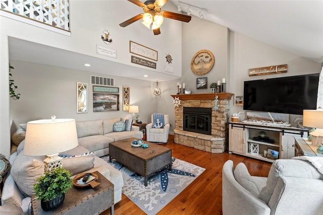 living room with hardwood / wood-style flooring, ceiling fan, a stone fireplace, and high vaulted ceiling