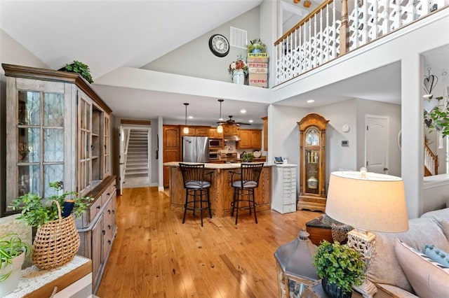 living room featuring ceiling fan, a high ceiling, and light hardwood / wood-style flooring