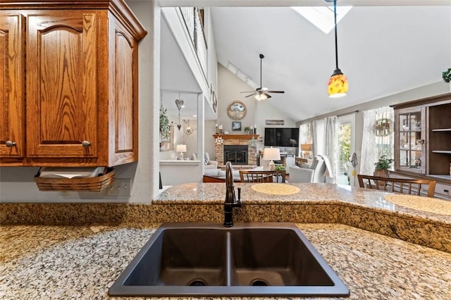 kitchen with a stone fireplace, sink, vaulted ceiling, ceiling fan, and decorative light fixtures