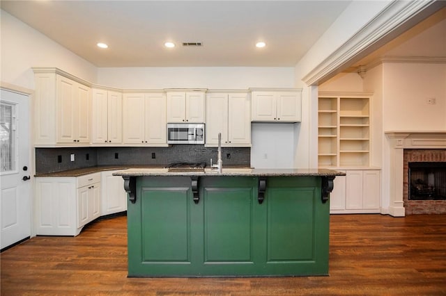 kitchen with a center island with sink, a kitchen breakfast bar, sink, dark stone countertops, and a fireplace