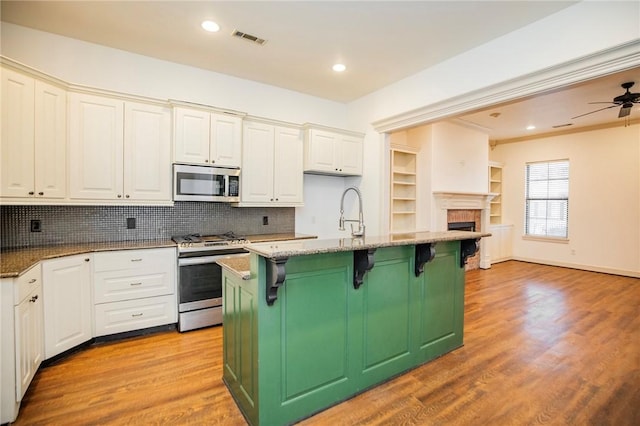 kitchen with ceiling fan, stainless steel appliances, stone countertops, a breakfast bar, and a center island with sink