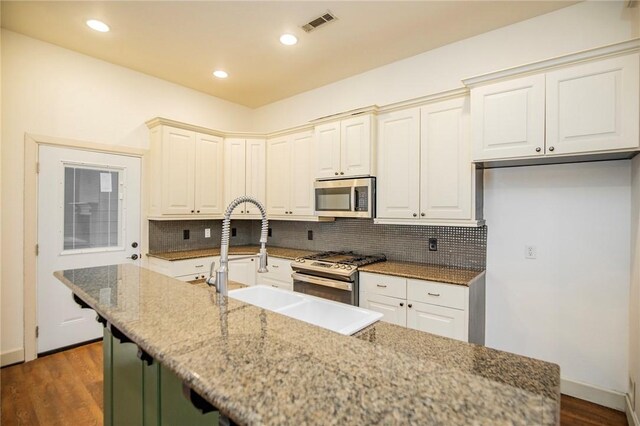 kitchen with dark wood-type flooring, a center island with sink, sink, appliances with stainless steel finishes, and light stone counters