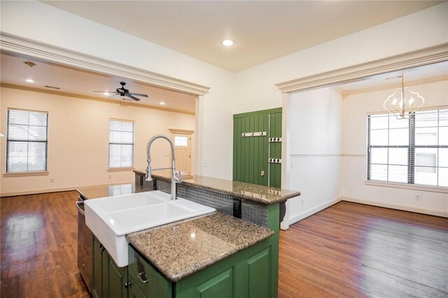 kitchen with ceiling fan with notable chandelier, green cabinets, sink, and an island with sink