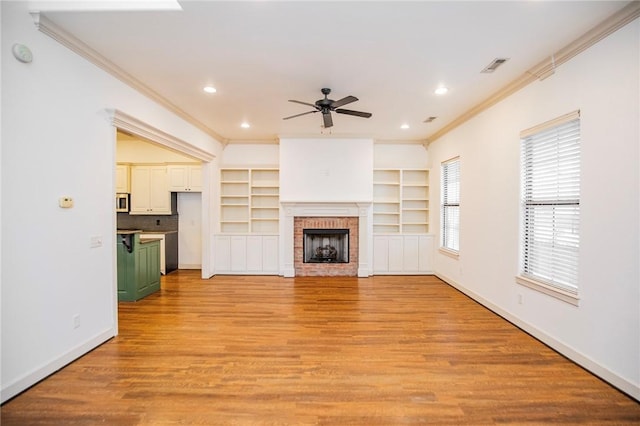 unfurnished living room with light hardwood / wood-style flooring, a brick fireplace, built in shelves, ceiling fan, and ornamental molding