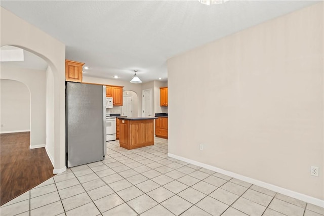 kitchen featuring stove, backsplash, light tile patterned floors, a kitchen island, and stainless steel refrigerator