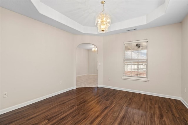 unfurnished room featuring a notable chandelier, dark hardwood / wood-style floors, and a raised ceiling