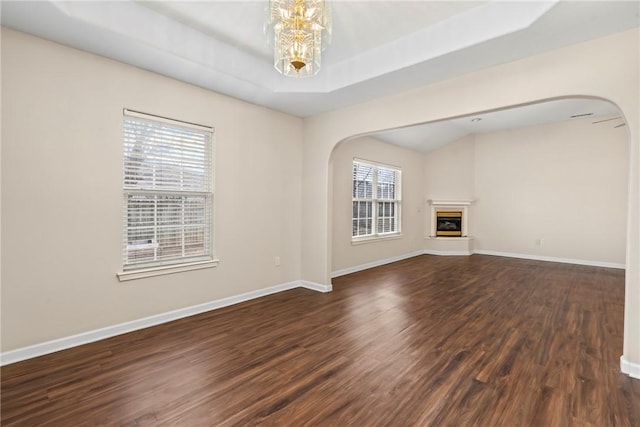 unfurnished living room featuring a raised ceiling, dark wood-type flooring, and a notable chandelier