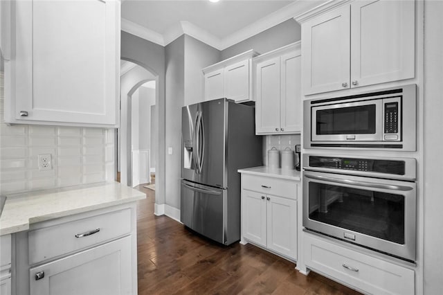 kitchen featuring light stone countertops, decorative backsplash, ornamental molding, stainless steel appliances, and white cabinetry