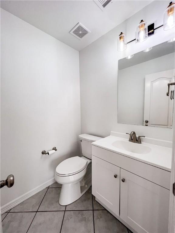 half bathroom featuring tile patterned flooring, toilet, vanity, visible vents, and baseboards