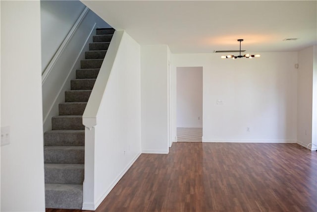 empty room with an inviting chandelier, baseboards, stairway, and dark wood-type flooring