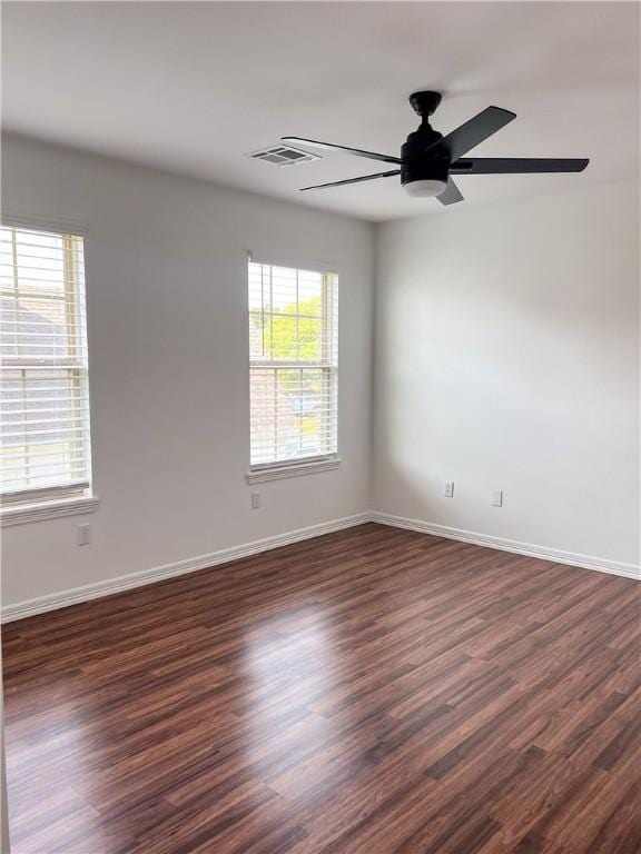 spare room with dark wood-style floors, visible vents, a ceiling fan, and baseboards