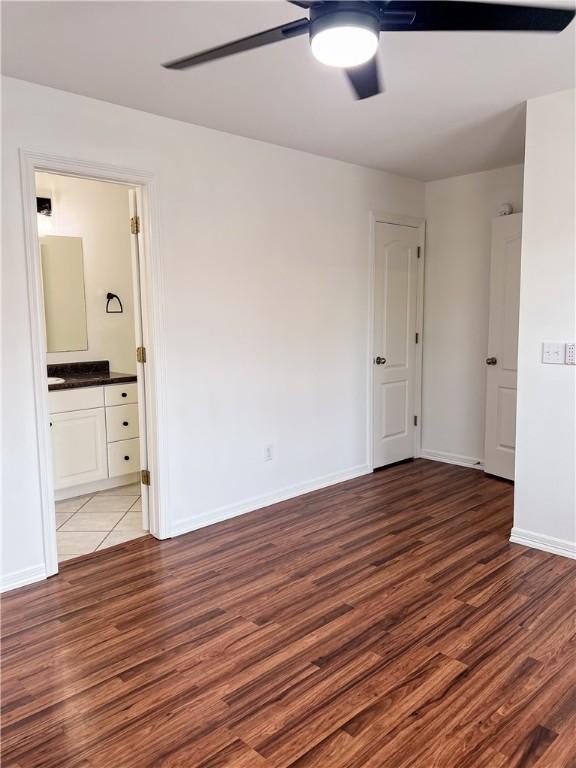 unfurnished bedroom featuring ensuite bathroom, ceiling fan, wood finished floors, and baseboards