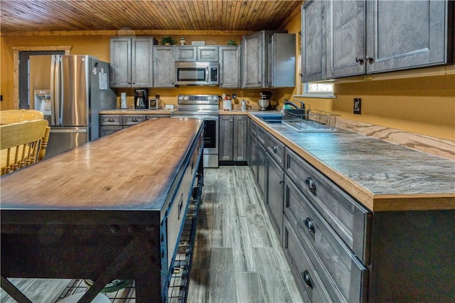 kitchen with stainless steel appliances, light wood-type flooring, a kitchen island, sink, and butcher block counters