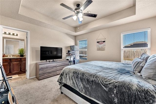 carpeted bedroom featuring a raised ceiling, ceiling fan, and connected bathroom