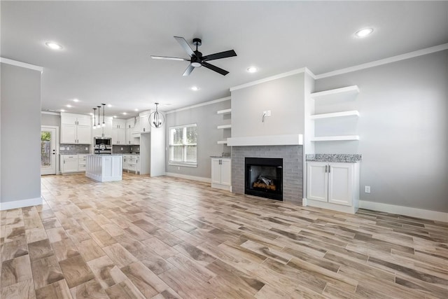 unfurnished living room featuring crown molding, a fireplace, ceiling fan with notable chandelier, and light wood-type flooring