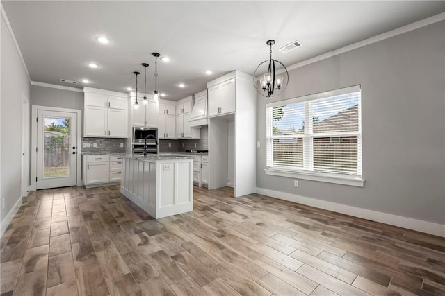 kitchen with light stone counters, a center island with sink, white cabinets, and hanging light fixtures