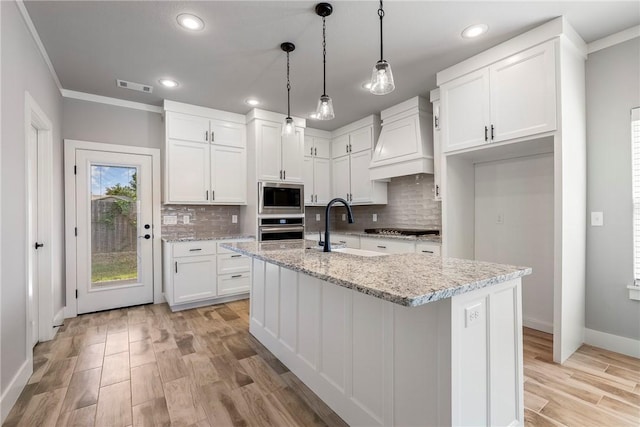 kitchen featuring custom range hood, stainless steel appliances, white cabinetry, and an island with sink