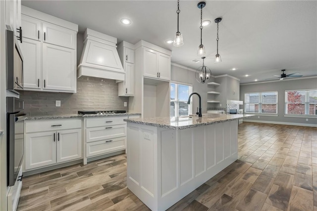 kitchen with a center island with sink, custom exhaust hood, pendant lighting, and white cabinetry