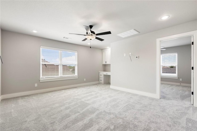 unfurnished living room featuring ceiling fan, built in desk, and light carpet