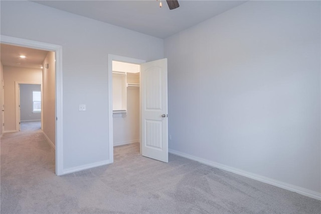 unfurnished bedroom featuring a walk in closet, ceiling fan, a closet, and light colored carpet