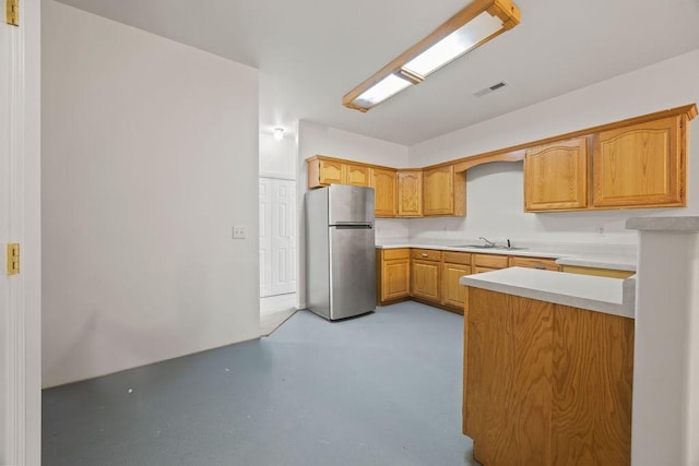 kitchen featuring light countertops, visible vents, freestanding refrigerator, a sink, and concrete flooring