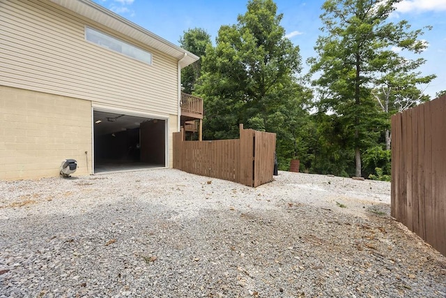 view of property exterior featuring driveway, an attached garage, and fence