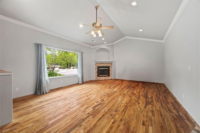 unfurnished living room featuring ceiling fan, wood finished floors, vaulted ceiling, a tiled fireplace, and crown molding