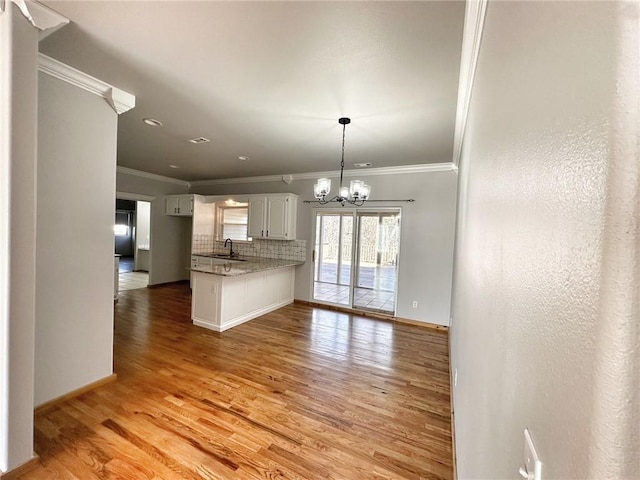 kitchen with decorative backsplash, a peninsula, light wood-style floors, a chandelier, and a sink